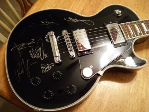 1997 Ford Probe - Black electric guitar with multiple silver signatures on its body, placed on a wooden surface.