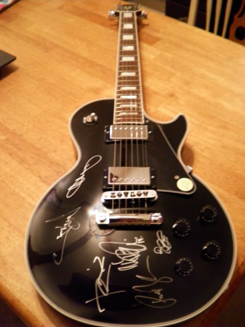 1997 Ford Probe - A black electric guitar with multiple signatures is displayed on a wooden surface.