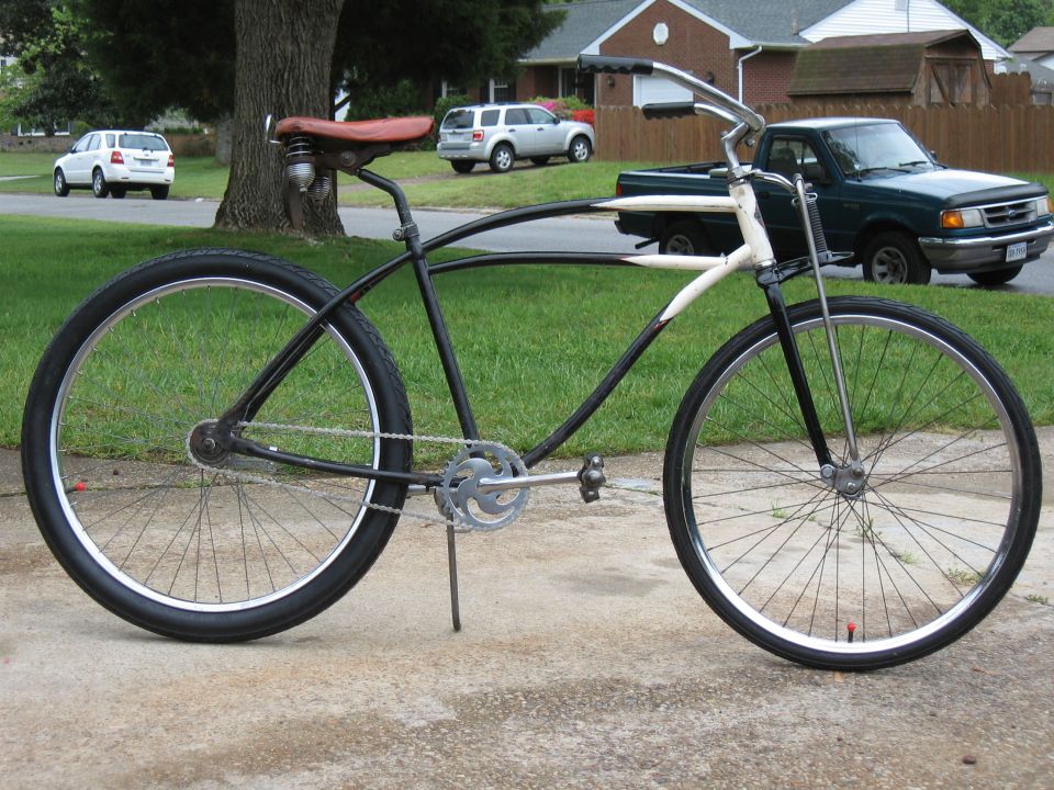 Cruiser bicycle parked on concrete with a green pickup truck and two SUVs in the background