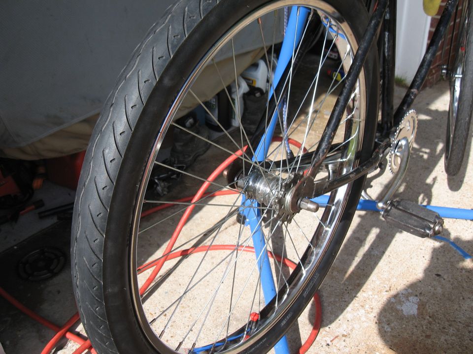 Bicycle rear wheel with chrome spokes and black tire on a blue stand