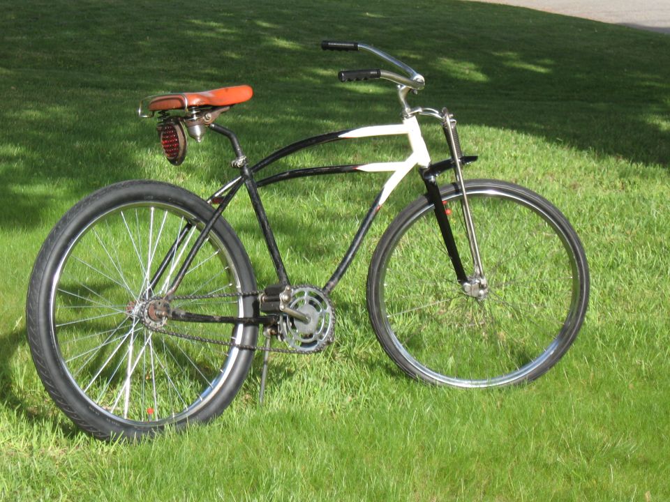 Black and white bicycle with a brown leather seat and a red taillight, parked on grass