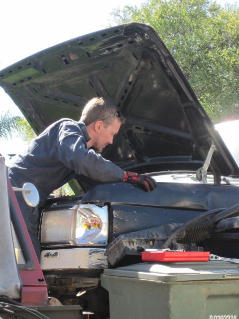1989 Ford Bronco - Mechanic works on the engine of a truck, which has a 4x4 badge on its front fender.