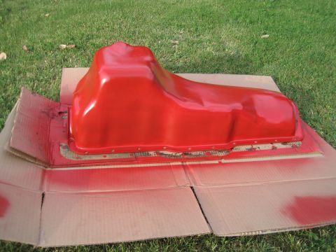 1989 Ford Bronco - A freshly painted red oil pan rests on cardboard, with overspray visible on the grass.