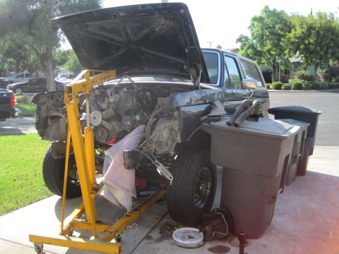 1989 Ford Bronco - The engine bay of a vehicle is shown with the engine removed and a hoist in place.