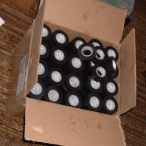 1986 Ford Bronco - A box overflows with numerous rolls of black electrical tape, ready for use.