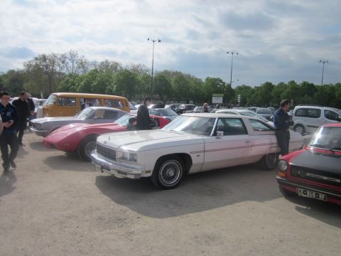 1991 Ford LTD Crown Victoria - A white coupe from 1977 is parked in a lot with other vehicles under a cloudy sky.