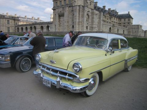 1991 Ford LTD Crown Victoria - A classic yellow and white Chevrolet sedan is parked in front of a large stone building.