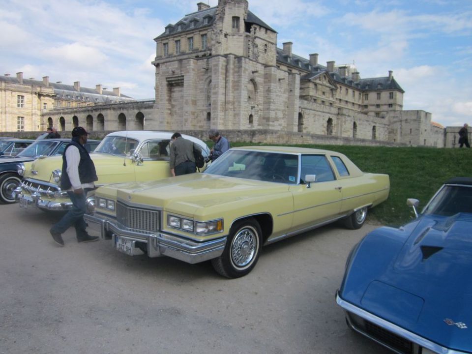 Yellow 1975 Cadillac Coupe DeVille parked in front of a castle