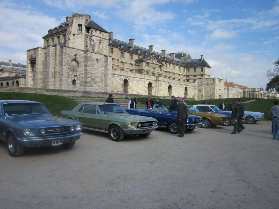 Several classic Ford Mustangs parked in front of a large stone building