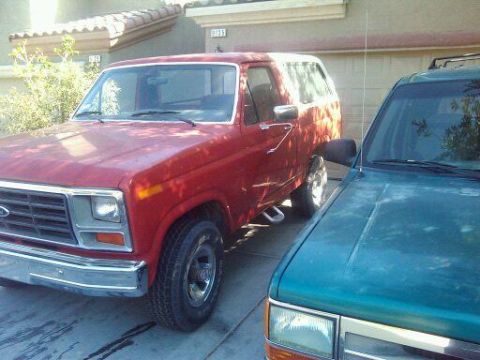 1985 Ford Bronco - A red 1985 Ford Bronco is parked next to a teal SUV in a driveway.