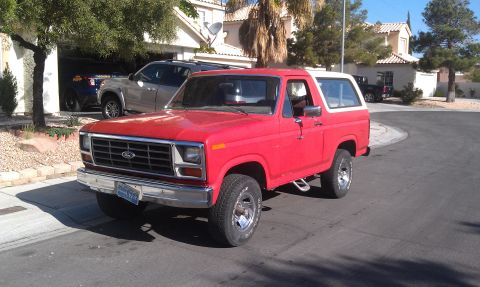 1985 Ford Bronco - A red Ford Bronco with a white top is parked on a street in front of a house.