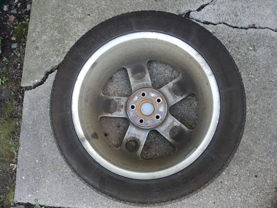 Car wheel with five spokes and a tire, resting on cracked concrete