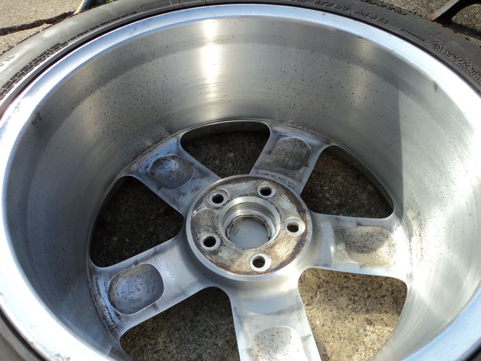 Aluminum wheel with five spokes, showing wear and dirt. A tire is partially visible