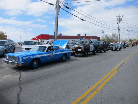 1991 Ford Crown Victoria - Several police vehicles are parked in a line on a street under a cloudy sky.
