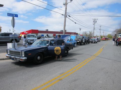 1991 Ford Crown Victoria - A line of police cars and other vehicles are parked on Beacon Street under a partly cloudy sky.