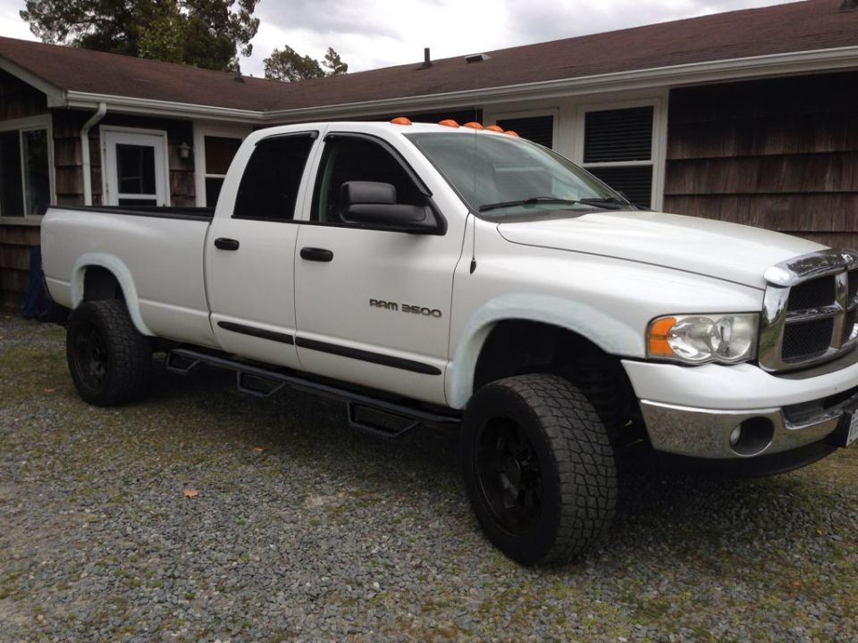 White Dodge Ram 3500 quad cab pickup with black wheels on gravel driveway