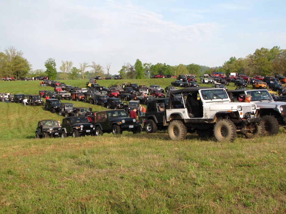 Many Jeeps parked on a grassy hill under a partly cloudy sky