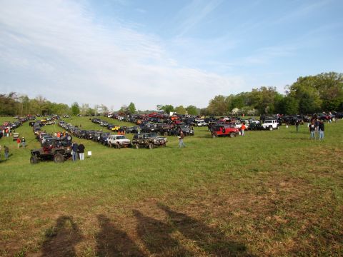 1979 Ford Bronco - A large gathering of off-road vehicles are parked in a grassy field under a partly cloudy sky.