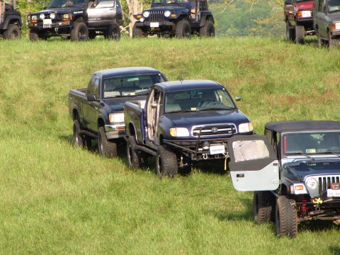 1979 Ford Bronco - A collection of modified off-road vehicles are gathered on a grassy incline, with a blue Toyota Tundra prominently featured.