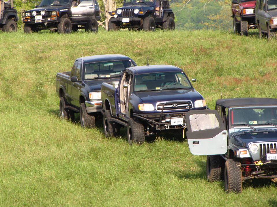 Several off-road vehicles parked on a grassy slope, including a blue Toyota Tundra and a Jeep Wrangler