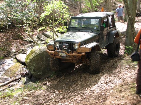 1979 Ford Bronco - A green Jeep Wrangler navigates a rocky trail in a wooded area.