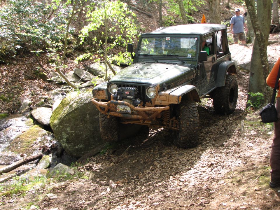 Green Jeep Wrangler off-roading over a large rock on a dirt path