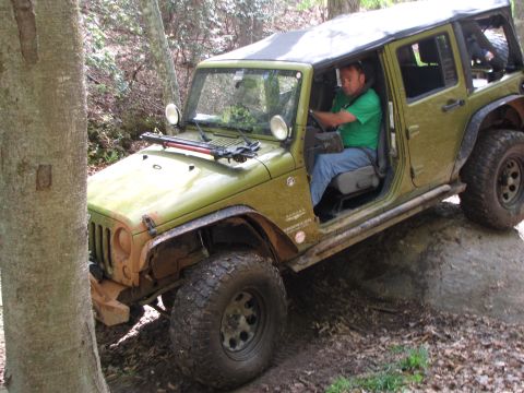 1979 Ford Bronco - A green Jeep Wrangler navigates a rocky trail with a driver inside.
