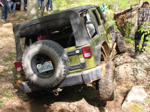 1979 Ford Bronco - A green Jeep Wrangler tackles a challenging off-road course, its spare tire prominently displayed on the rear.