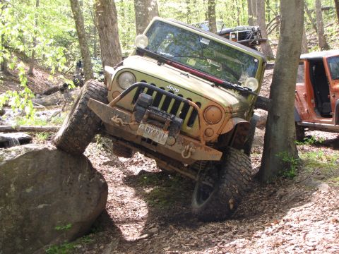 1979 Ford Bronco - Jeep Wrangler navigating a difficult off-road obstacle on a forest trail.