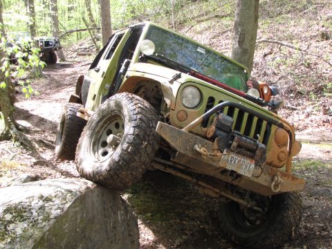 1979 Ford Bronco - A Jeep navigates a rocky obstacle on a wooded trail, with another vehicle following behind.