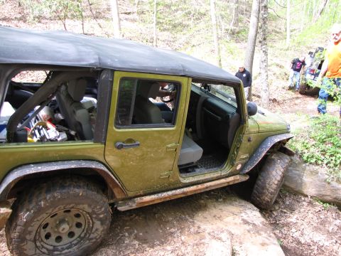 1979 Ford Bronco - A green Jeep Wrangler is shown off-roading with its doors removed, while other vehicles and people are visible in the background.