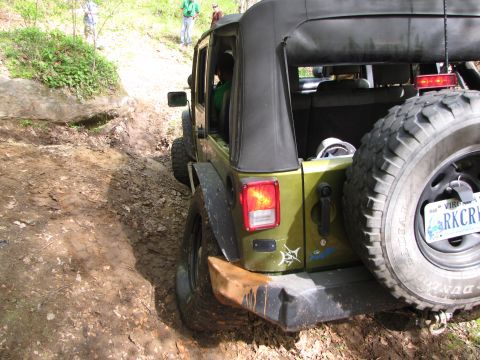 1979 Ford Bronco - Jeep Wrangler navigating a muddy trail with people watching in the background.