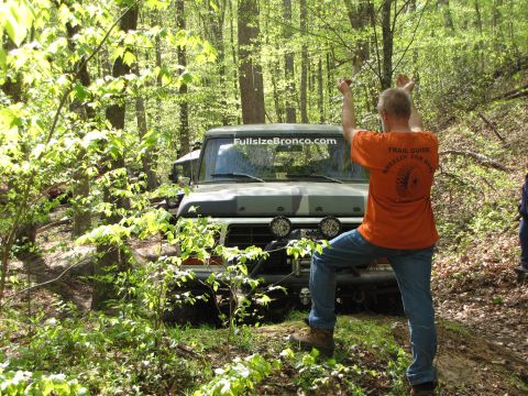 1979 Ford Bronco - A man in an orange shirt stands in front of a camouflaged Ford Bronco in a wooded area.