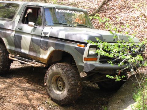 1979 Ford Bronco - This 1979 Ford Bronco is shown in a three-quarter front view, navigating an off-road trail with camouflage paint.