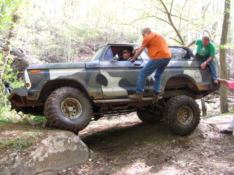 1979 Ford Bronco - A camouflaged Ford Bronco is being used for off-roading, with several people interacting with the vehicle as it traverses rough terrain.
