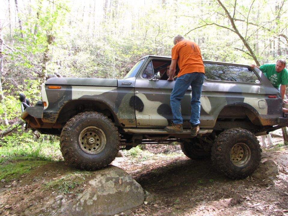 Camouflaged 1978 Ford Bronco off-roading with two men near the doors