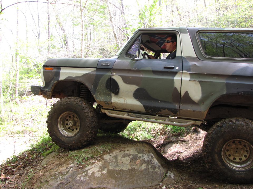 Camouflaged Ford Bronco with lifted suspension and large tires navigating rocky terrain