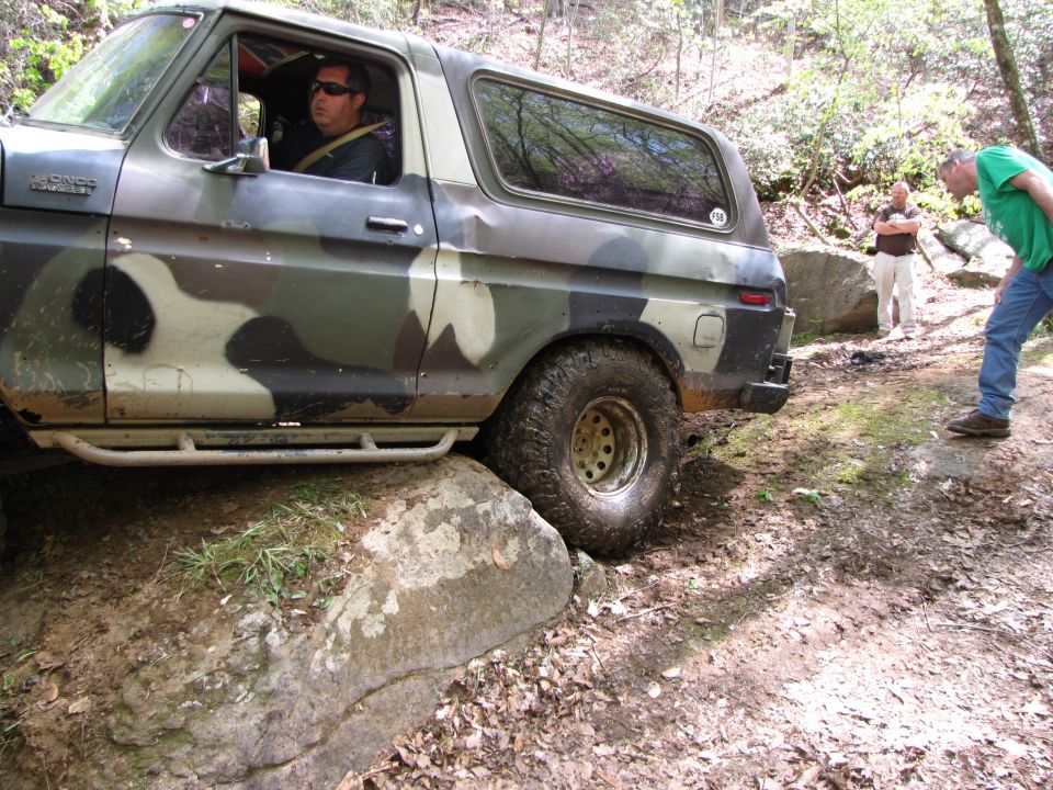 Man driving a camouflage 1979 Ford Bronco over rocks on a trail