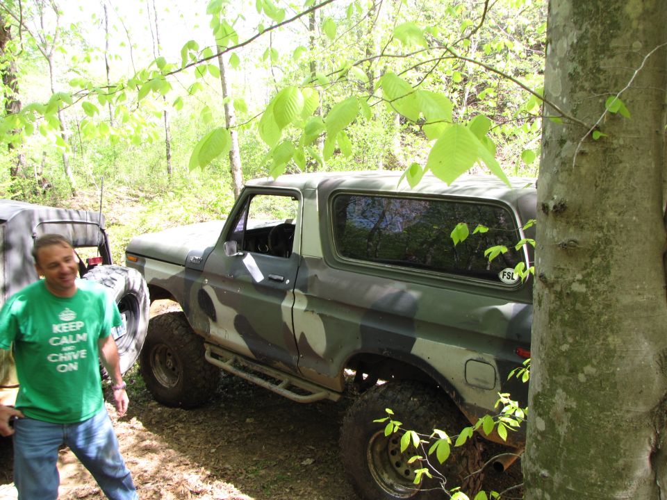 1979 Ford Bronco, camouflage paint, 3/4 front view, parked in woods
