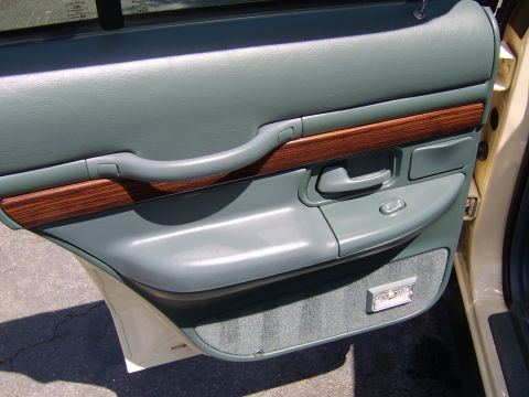 1996 Mercury Grand Marquis - The interior door panel of a car features gray upholstery, wood grain accents, and a speaker grille.
