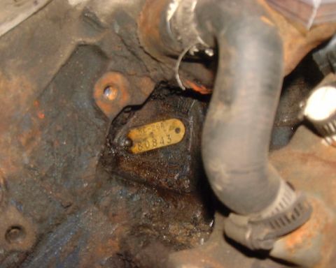 1985 Ford F-150 - Close-up of an engine block with a stamped metal identification tag and a rubber hose attached.