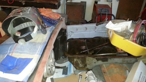 2005 Ford Mustang - A welding mask rests on a blanket next to various car parts, including an oil pan, in a disorganized garage setting.