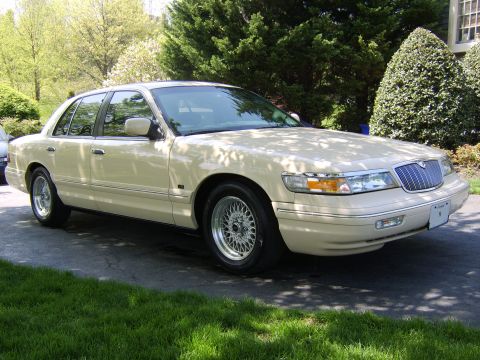 1996 Mercury Grand Marquis - Tan 1996 Mercury Grand Marquis sedan parked on a paved driveway with green grass and trees in the background.