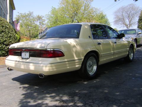 1996 Mercury Grand Marquis - A tan 1996 Mercury Grand Marquis is parked on a residential street, showing its rear profile and chrome accents.