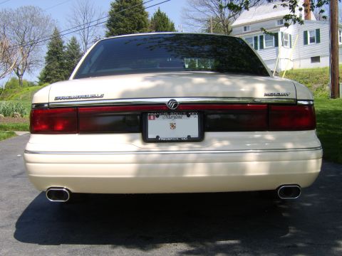 1996 Mercury Grand Marquis - The rear of a cream-colored Mercury Grand Marquis is shown, its taillights, license plate, and dual exhaust pipes.
