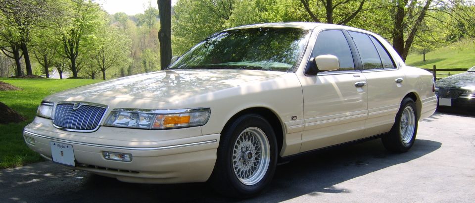 Cream Mercury Grand Marquis sedan front 3/4 view, wide crop, on paved drive