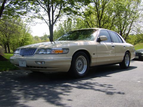 1996 Mercury Grand Marquis - Tan 1996 Mercury Grand Marquis sedan parked on asphalt with trees in the background.