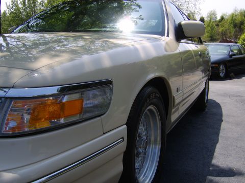 1996 Mercury Grand Marquis - A close-up view of the front passenger side of a cream-colored sedan, with another dark sedan in the background.