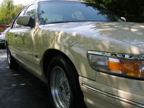 1996 Mercury Grand Marquis - A tan sedan is viewed from the front quarter angle, showing its fender, headlight, and wire wheels.
