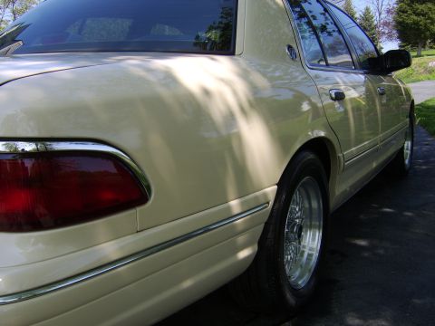 1996 Mercury Grand Marquis - Rear side view of a cream-colored sedan with chrome accents and aftermarket wheels.